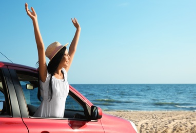 Happy young woman leaning out of car window on beach, space for text. Summer trip