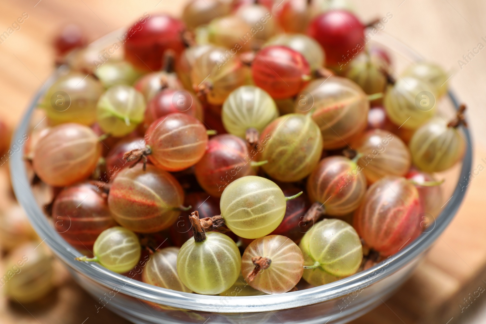 Photo of Glass bowl with fresh ripe gooseberries on table, closeup
