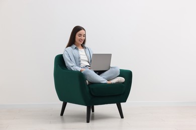 Photo of Beautiful woman using laptop while sitting in armchair near white wall indoors