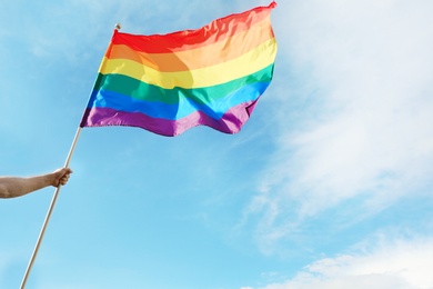 Photo of Gay man holding rainbow LGBT flag against blue sky. Space for text