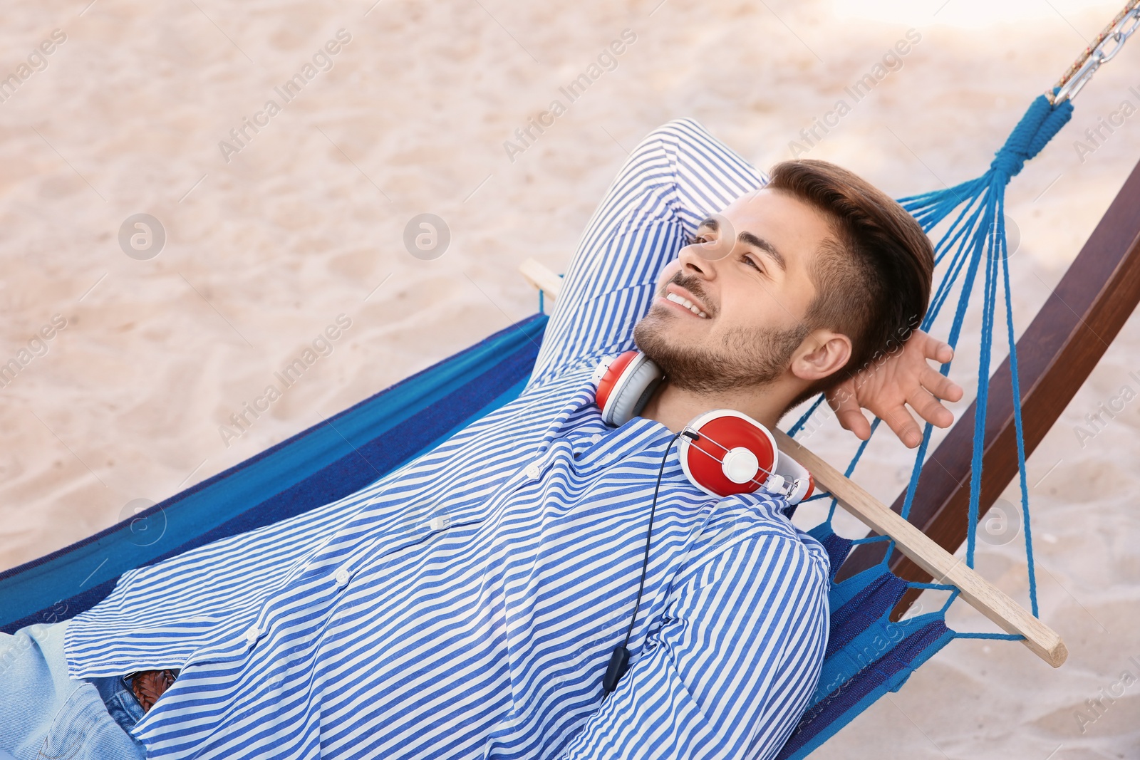 Photo of Young man with headphones resting in hammock at seaside