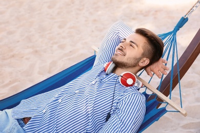 Young man with headphones resting in hammock at seaside