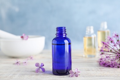 Photo of Bottle of essential oil with flowers on wooden table against color background