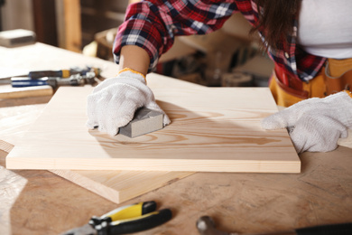 Photo of Female carpenter polishing wooden board in workshop, closeup