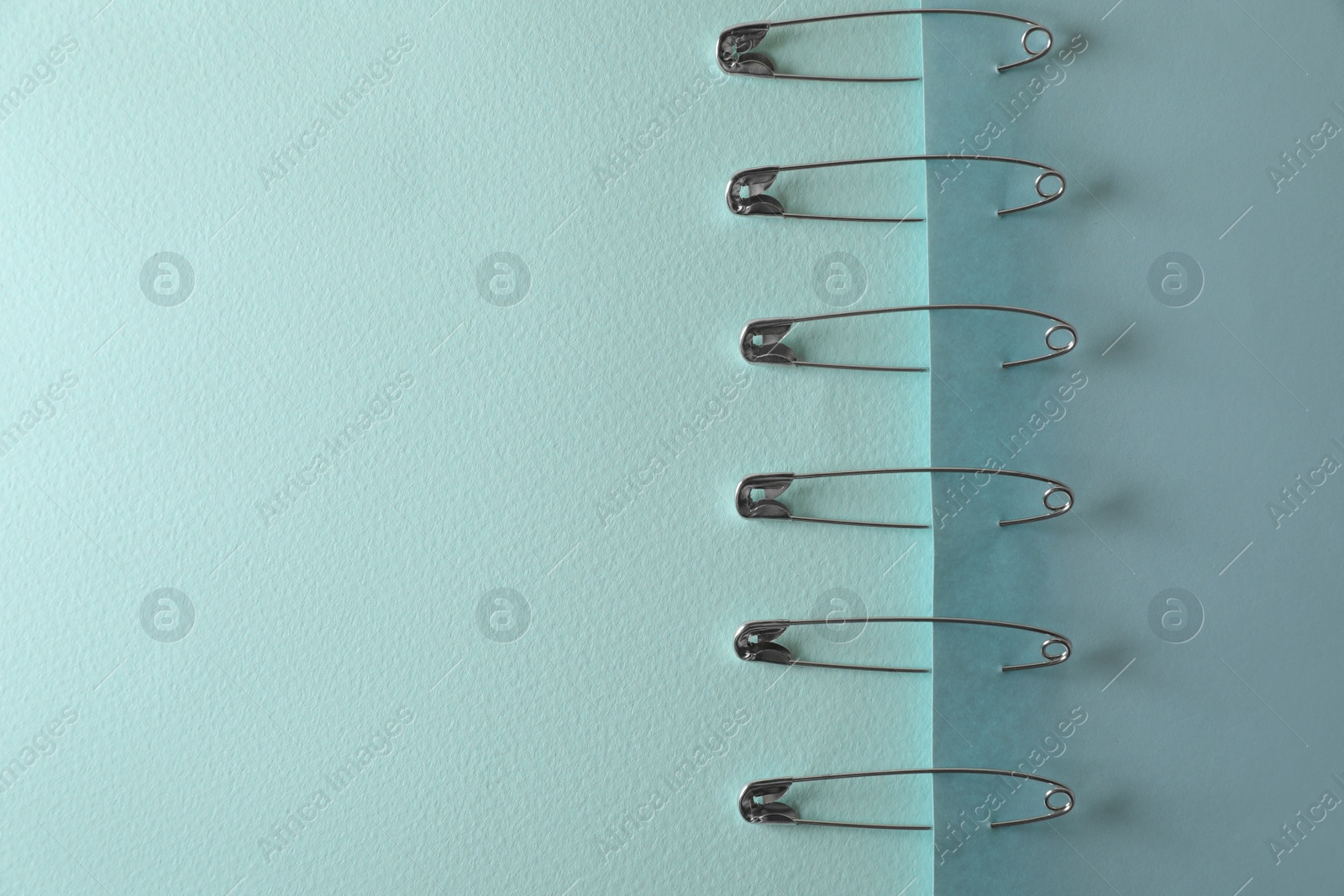 Photo of Many safety pins on light blue paper, flat lay. Space for text