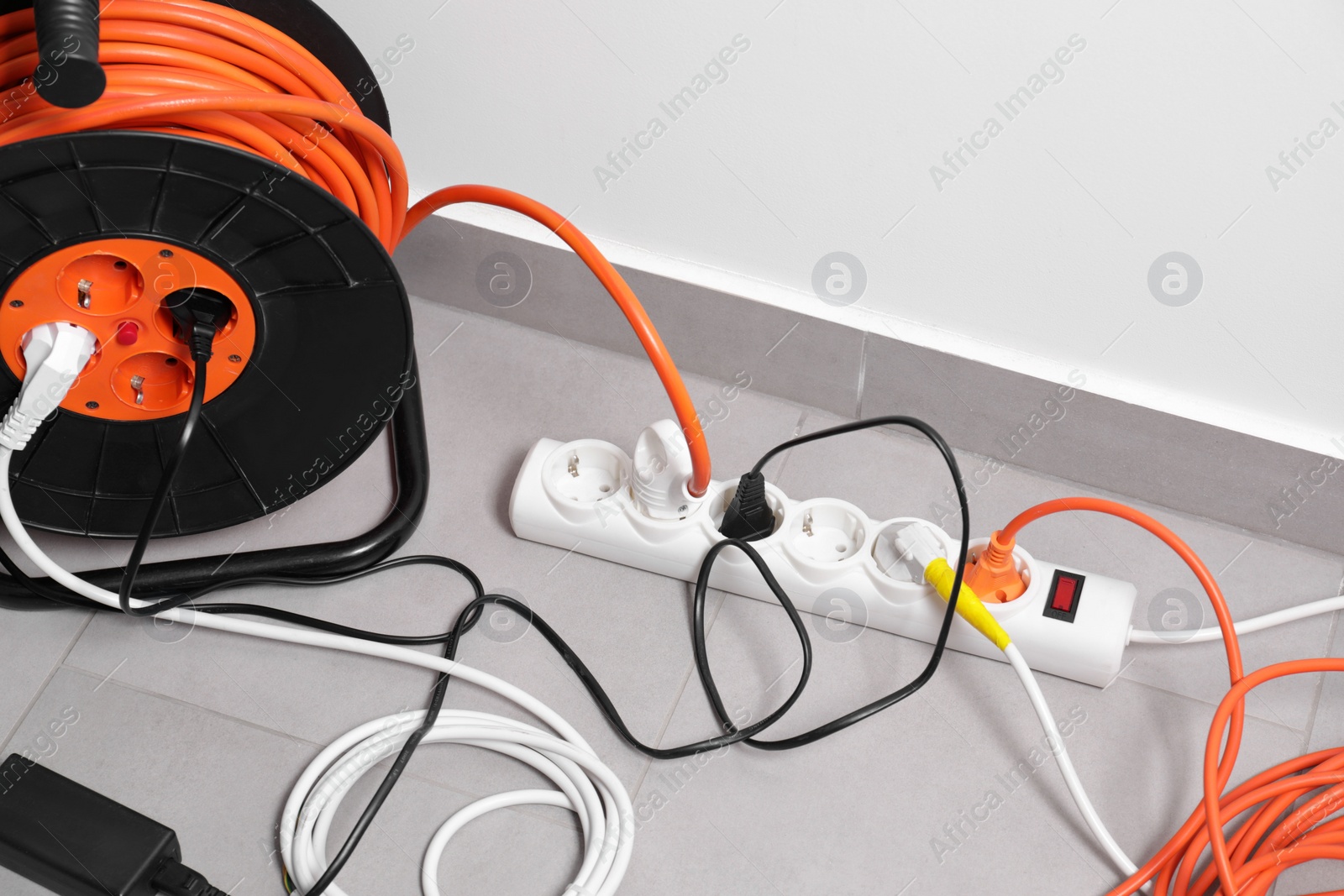 Photo of Extension cord reel plugged into power strip on grey floor indoors, space for text