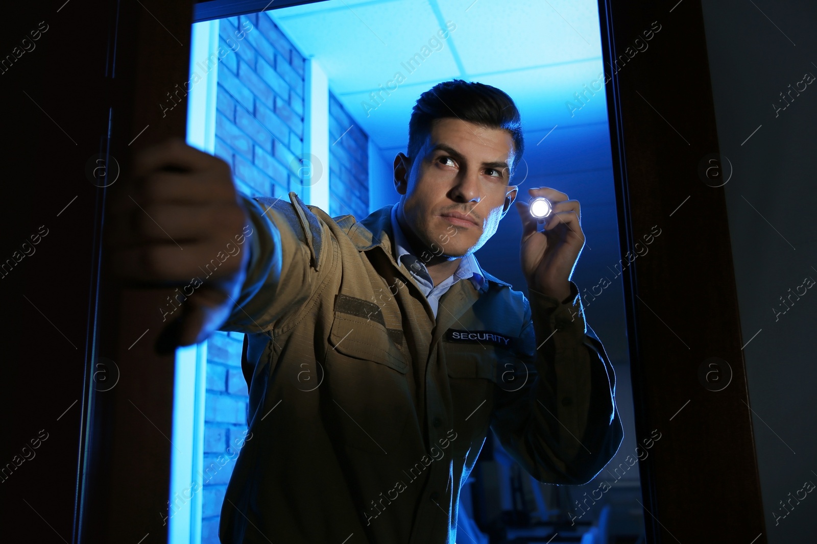 Photo of Professional security guard with flashlight checking dark room