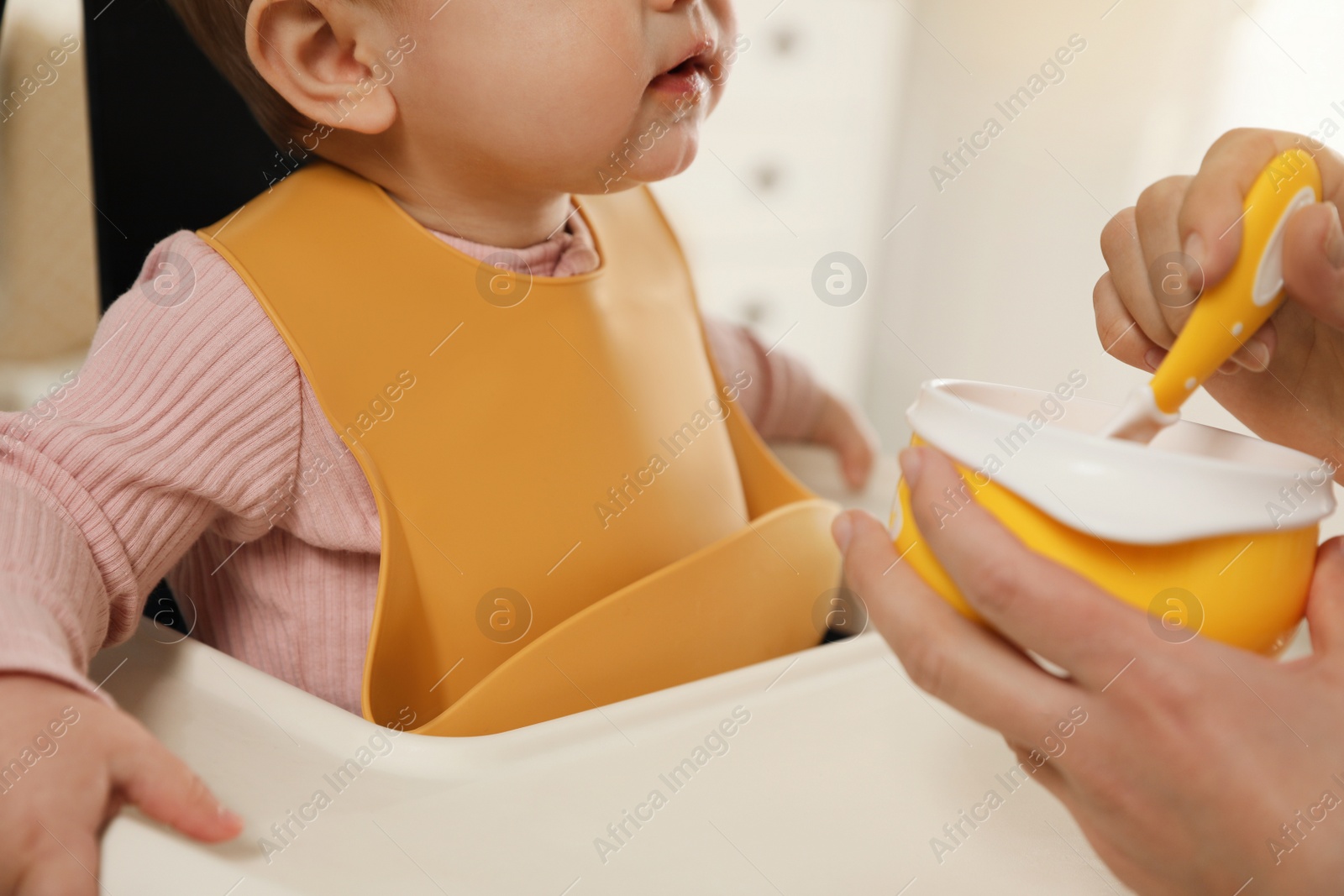 Photo of Mother feeding her little baby indoors, closeup. Kid wearing silicone bib