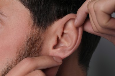 Man touching his ear on grey background, closeup
