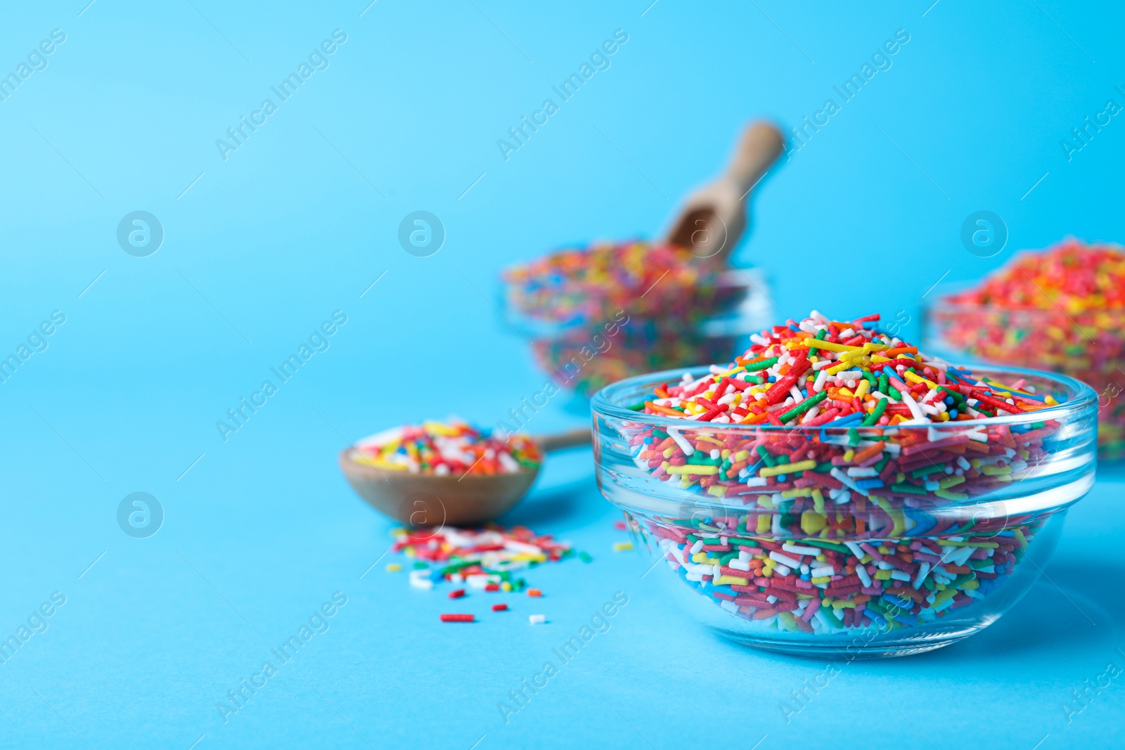 Photo of Colorful sprinkles in bowl on light blue background, space for text. Confectionery decor