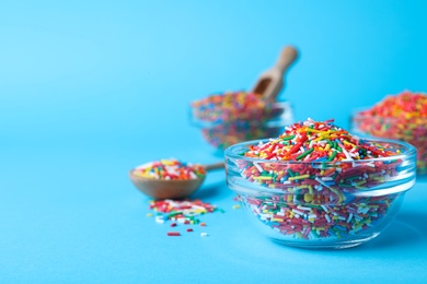 Photo of Colorful sprinkles in bowl on light blue background, space for text. Confectionery decor