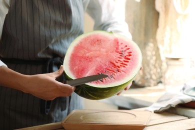 Photo of Woman cutting fresh juicy watermelon above wooden table, closeup