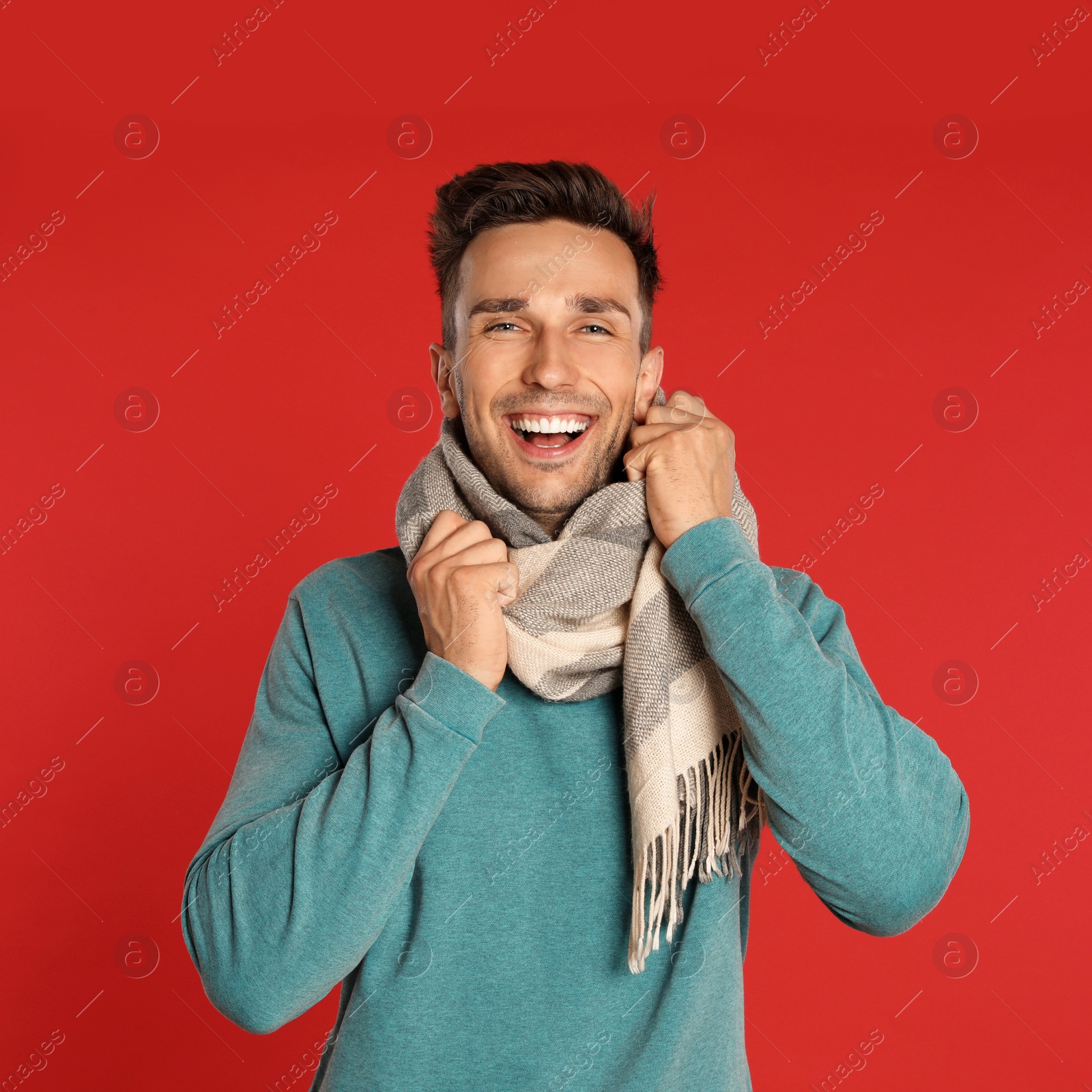 Photo of Happy young man in scarf and sweatshirt on red background. Winter season