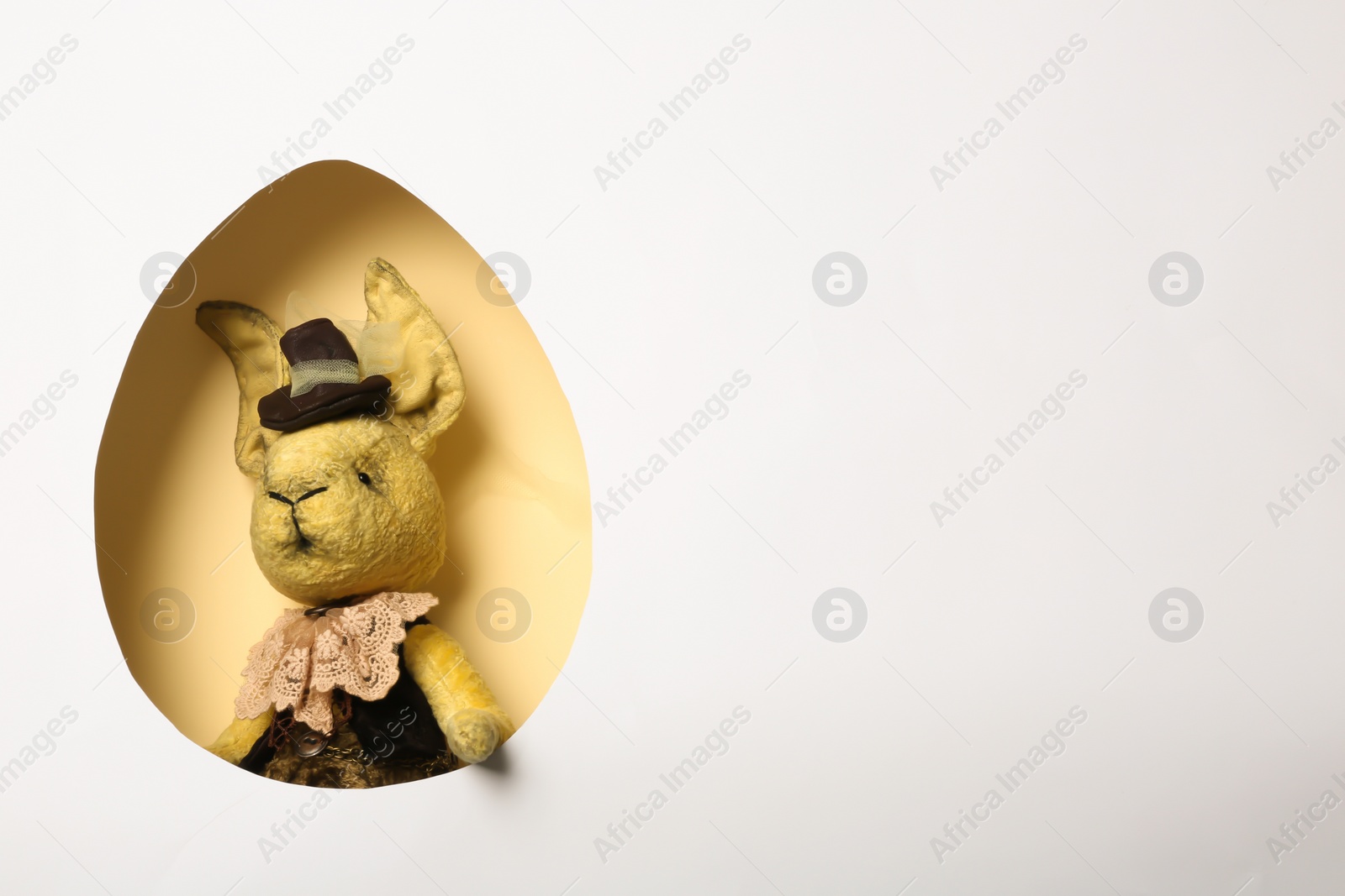 Photo of View of vintage Easter bunny toy on color background through egg shaped hole, top view. Space for text