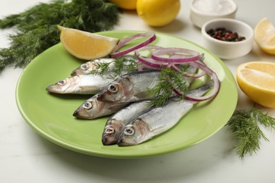 Photo of Fresh raw sprats, dill, lemon and onion on white table, closeup