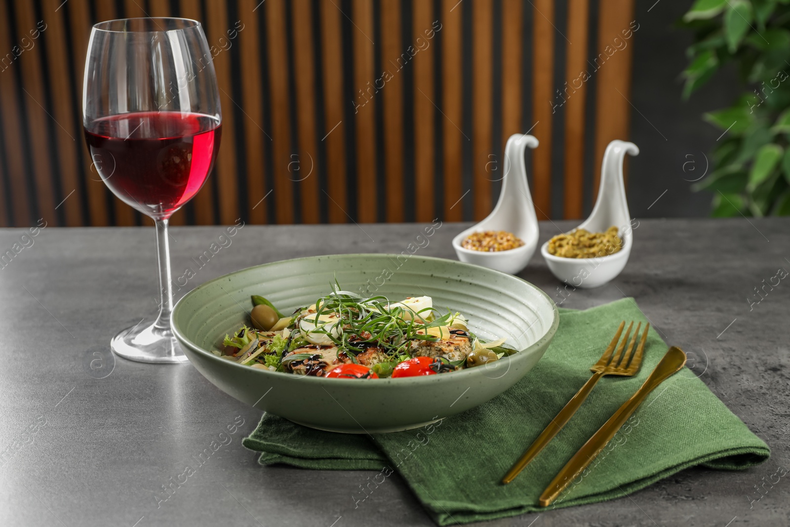 Photo of Tasty dish with tarragon, salad dressings and glass of wine served on grey table