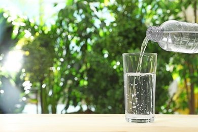 Photo of Pouring water from bottle into glass against blurred background, space for text. Refreshing drink