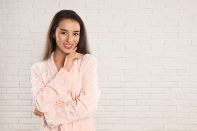 Photo of Beautiful young woman in bathrobe near white brick wall. Space for text