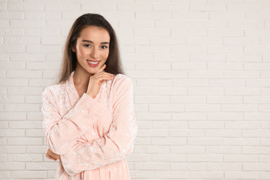 Beautiful young woman in bathrobe near white brick wall. Space for text