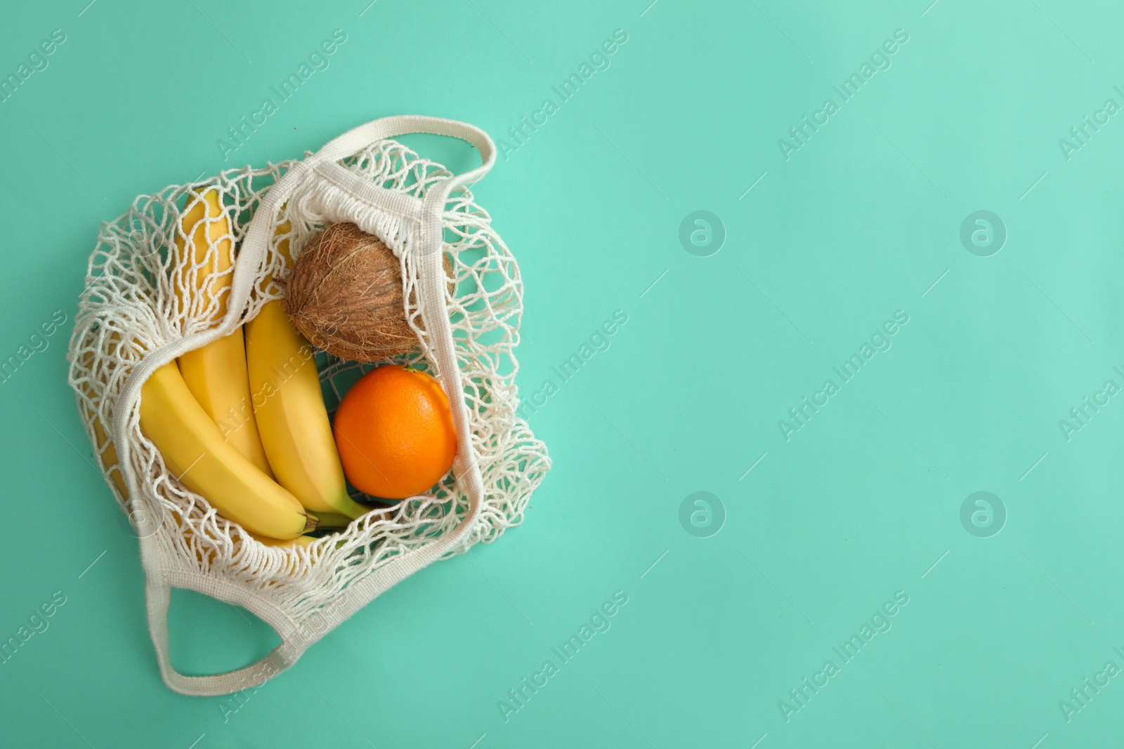 Photo of Net bag with fruits on turquoise background, top view. Space for text
