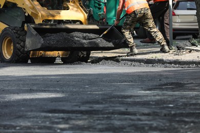 Photo of Worker laying new asphalt with skid loader on city street, closeup. Road repair service