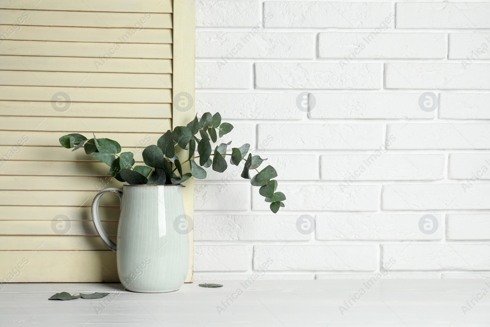 Photo of Beautiful eucalyptus branches in vase on white wooden table. Space for text