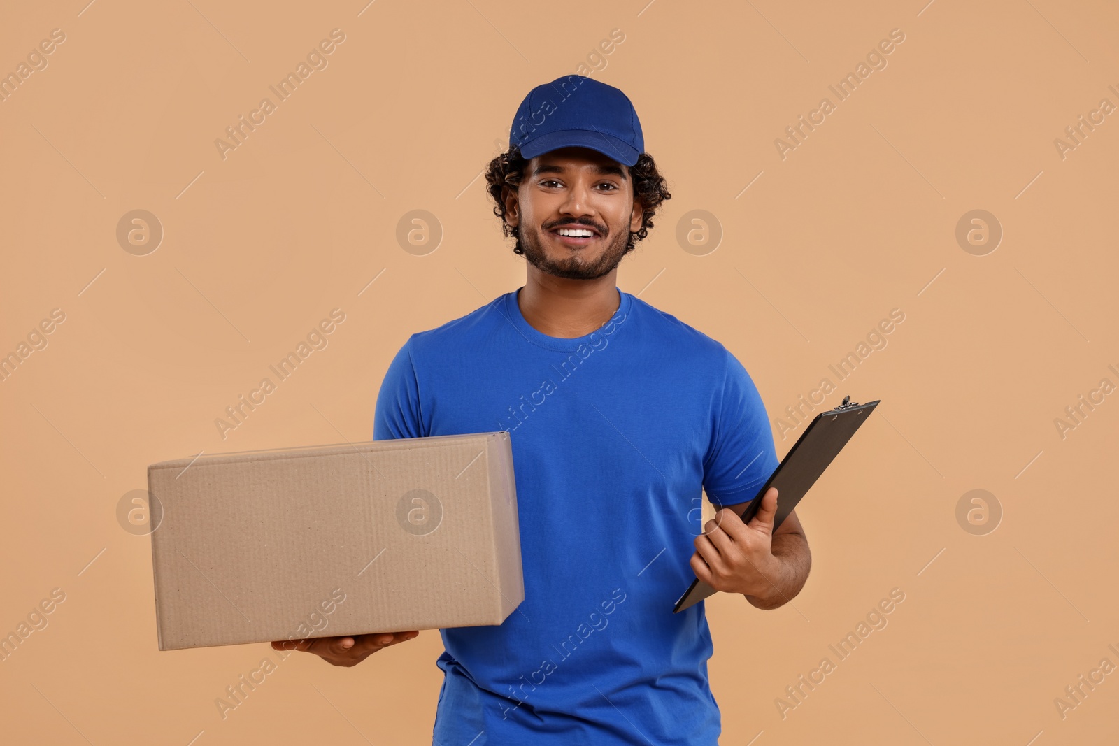 Photo of Happy courier with parcel and clipboard on light brown background