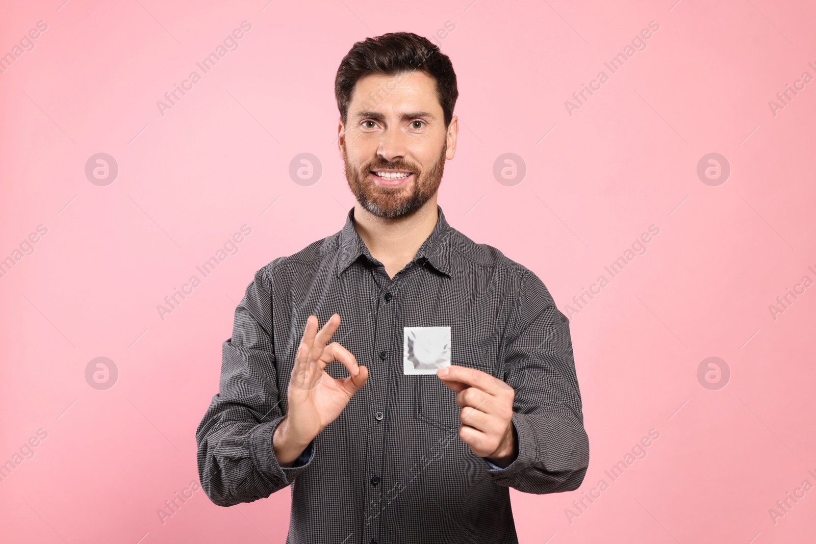 Photo of Happy man with condom showing ok gesture on pink background. Safe sex