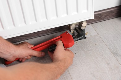 Professional plumber using adjustable wrench for installing new heating radiator indoors, closeup