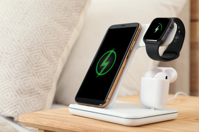Photo of Different gadgets charging on wireless pad in bedroom, closeup
