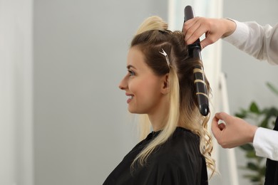 Hair styling. Hairdresser curling woman's hair in salon, closeup. Space for text