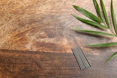Photo of Acupuncture needles and leaf on wooden table, flat lay. Space for text