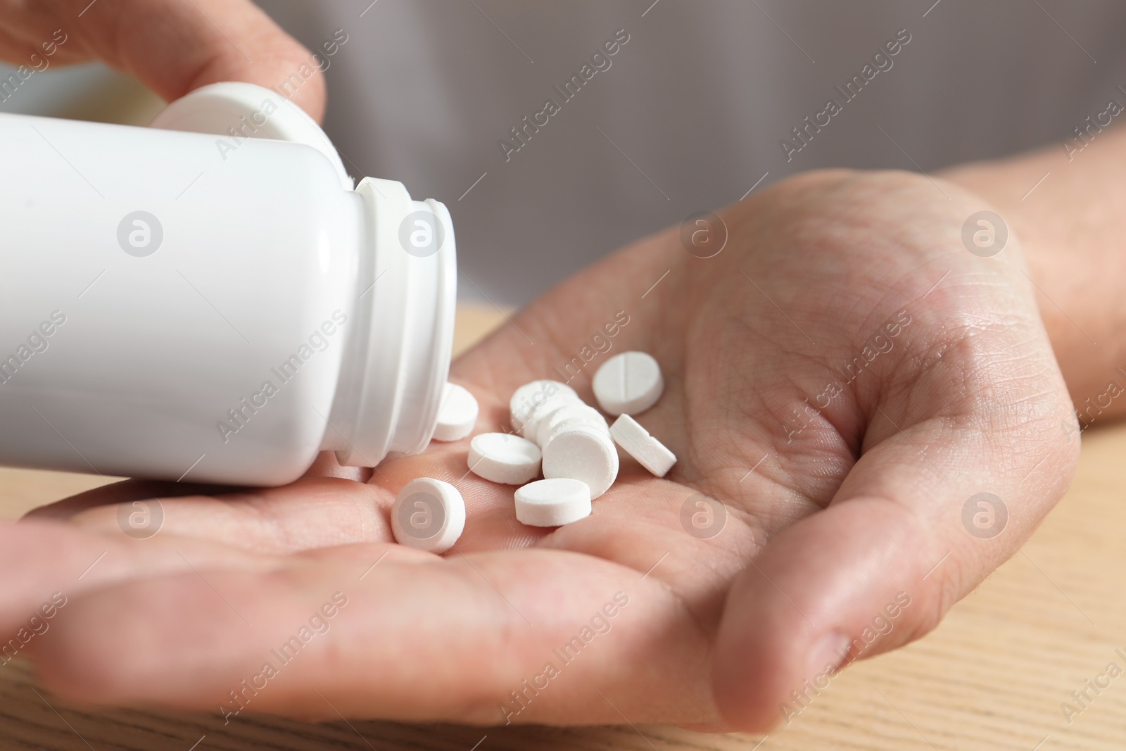 Photo of Man pouring pills from bottle at table, closeup