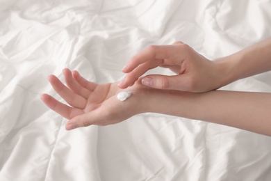 Photo of Young woman applying cream onto hands, indoors