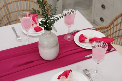 Photo of Table setting. Glasses of tasty beverage, plates, pink napkins and vase with green branches in dining room