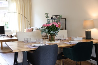 Photo of Beautiful table setting with bouquet in dining room. Roses and eucalyptus branches in vase