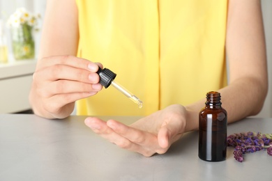 Photo of Woman applying essential oil on palm at table, closeup