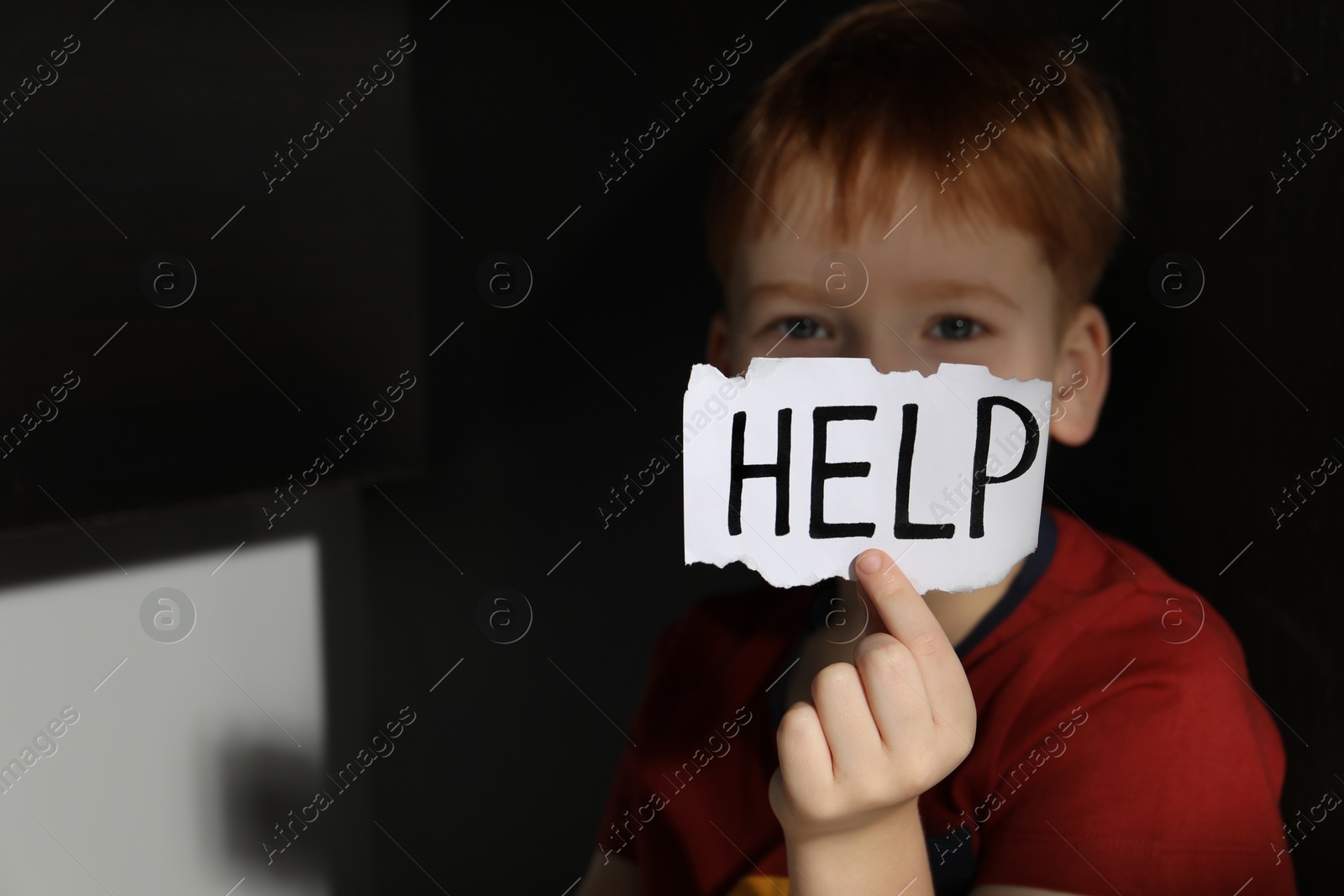Photo of Little boy holding piece of paper with word Help under table, closeup and space for text. Domestic violence concept