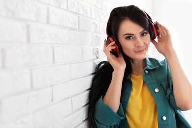 Photo of Portrait of beautiful woman listening to music with headphones near brick wall. Space for text