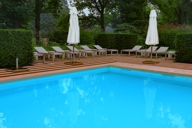 Photo of Many sunbeds and umbrellas near outdoor swimming pool