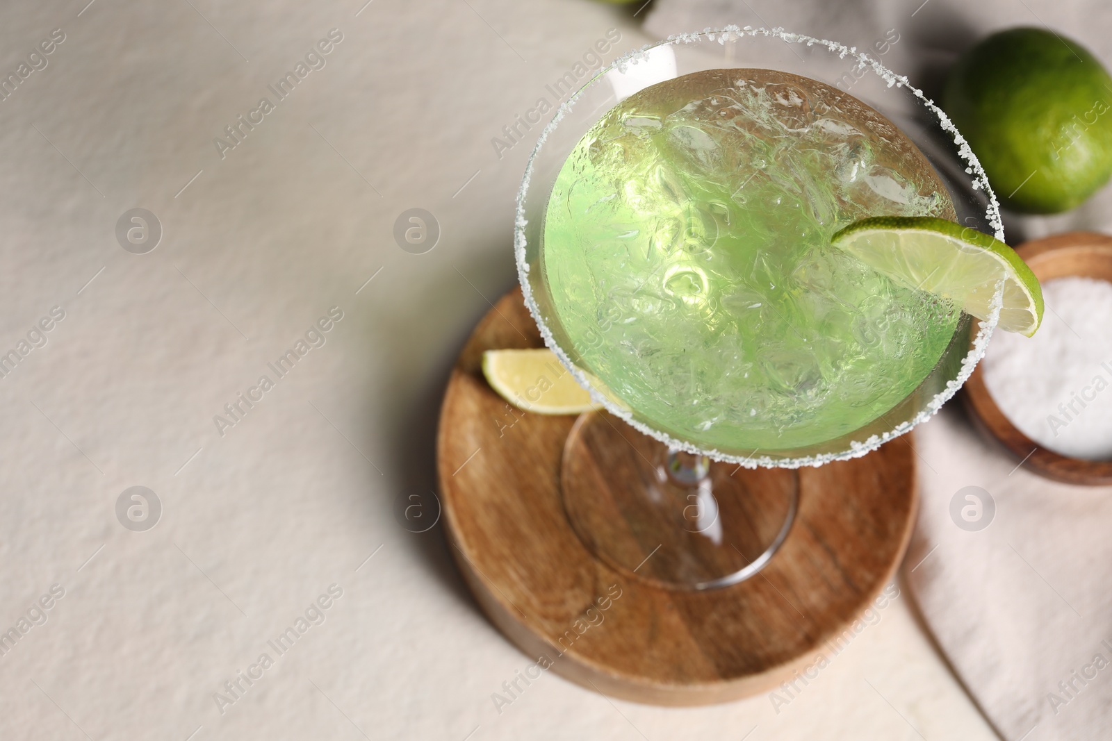 Photo of Delicious Margarita cocktail in glass, salt and limes on light table, above view. Space for text