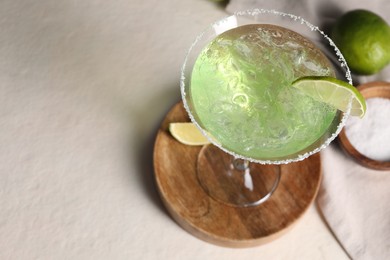 Photo of Delicious Margarita cocktail in glass, salt and limes on light table, above view. Space for text