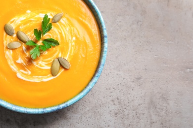 Bowl of tasty pumpkin soup and space for text on gray table, top view