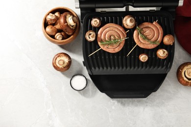 Photo of Electric grill with homemade sausages, rosemary and mushrooms on marble table, flat lay. Space for text