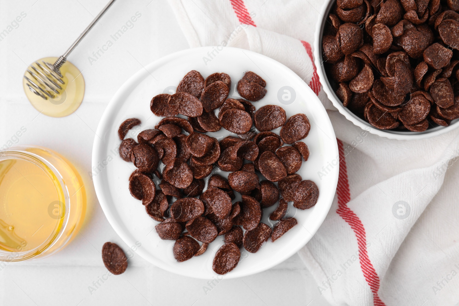 Photo of Breakfast cereal. Chocolate corn flakes and milk in bowl on white tiled table, flat lay