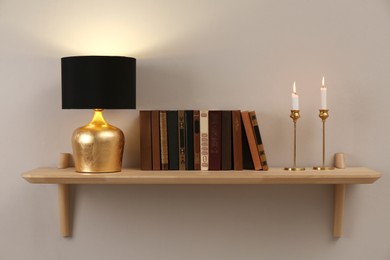 Wooden shelf with different books, burning candles and lamp on light wall