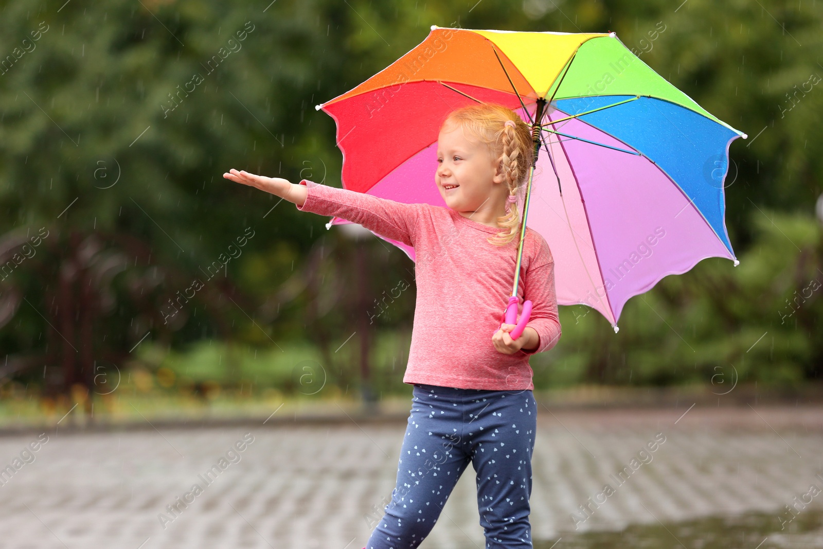 Photo of Cute little girl with bright umbrella under rain on street