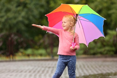 Photo of Cute little girl with bright umbrella under rain on street