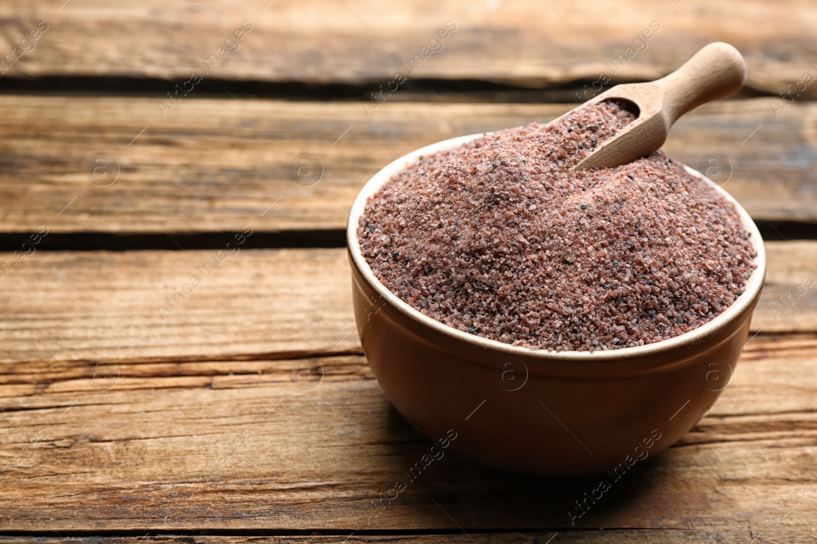 Photo of Ground black salt in bowl with scoop on wooden table. Space for text