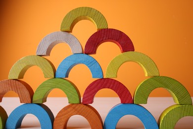 Photo of Colorful wooden pieces of educational toy on light table against orange wall, closeup. Motor skills development